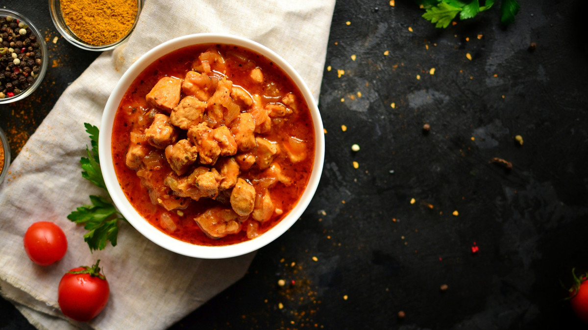 Dish of Indian Cuisine Tikka Masala. Chicken meat in tomato underpouring. Tikka Masala in a white pyalka on a dark background, a view from above, a place for text. Dark background. Linen napkin.