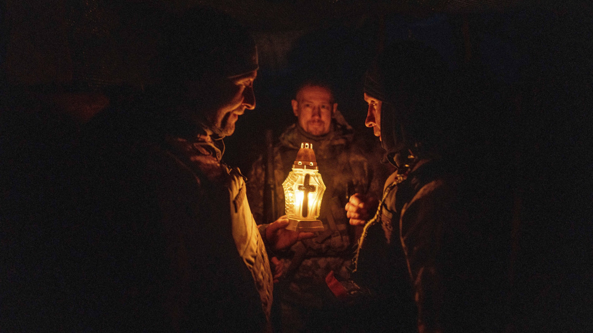 Ukrán katonák fohászkodnak a bajtársaik egyike által hozzájuk is eljuttatott betlehemi békeláng körül a kelet-ukrajnai Harkiv nagyváros térségében 2022. december 26-án.