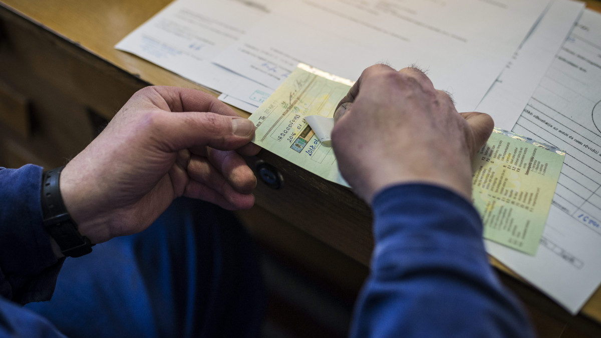 Sorszámcsíkot ragasztanak egy forgalmi engedélybe a műszaki vizsga végén egy tatabányai vizsgahelyen 2016. január 12-én. Idén januártól változott a műszaki vizsga rendje, kötelező lett az előminősítő vizsga. Azok a gépkocsik, amelyek ezen nem felelnek meg, nem is kerülhetnek a vizsgabiztosok elé.