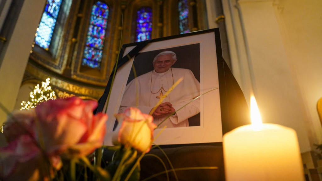 31 December 2022, Hamburg: A photo of Pope Emeritus Benedict XVI stands next to roses and a candle in St. Marys Cathedral. Pope Emeritus Benedict XVI died Dec. 31, 2022, at the Vatican at the age of 95. Photo: Marcus Brandt/dpa (Photo by Marcus Brandt/picture alliance via Getty Images)