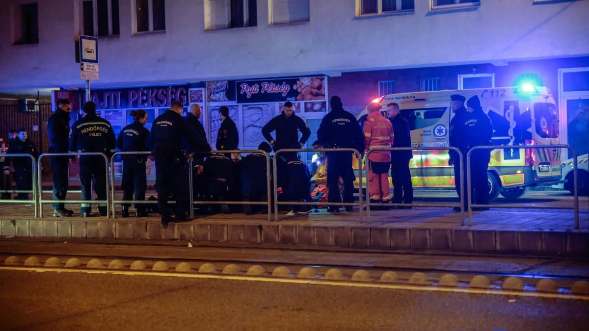 Rendőrök és mentők az elkövető körül Budapest XI. kerületében, egy Lecke utcai társasház előtt 2023. január 12-én éjjel. Három intézkedő rendőrt késsel sebesített meg egy támadó Újbudán, egyikük belehalt sérüléseibe. A támadót elfogták.
