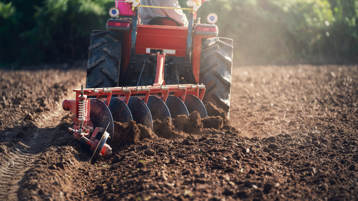 Agricultural worker with tractor preparing land with seedbed cultivator as part of pre seeding activities in early spring season of agricultural works at field, agricultural industry concept