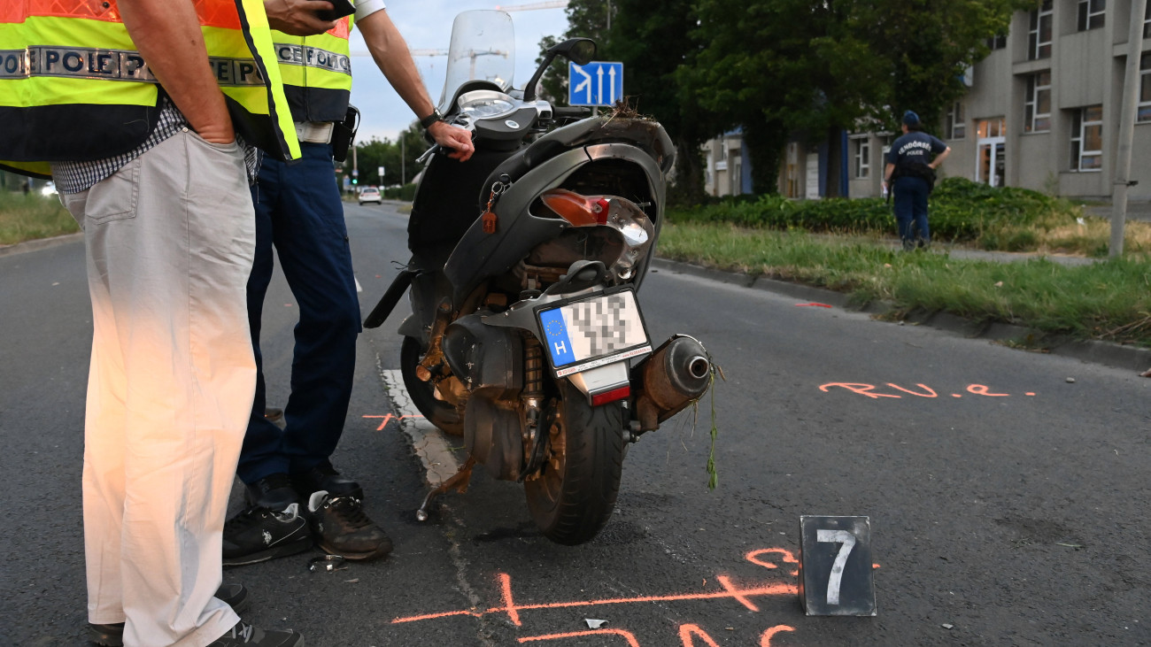 Összetört motorkerékpár mellett helyszínelnek rendőrök a főváros XI. kerületében, a Budafoki út és a Hengermalom út kereszteződésében 2023. június 24-én. A jármű autóval ütközött, a motort vezető férfi meghalt.