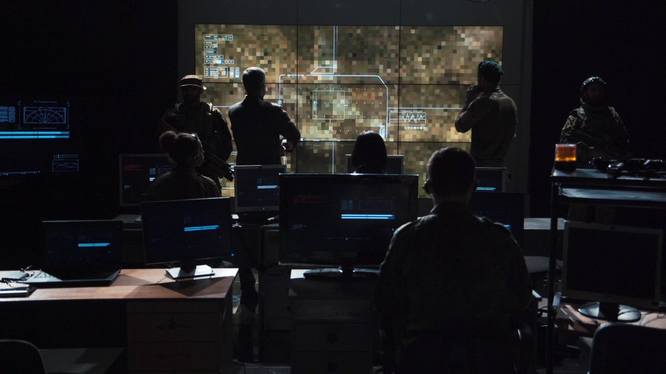 Group of soldiers or spies in dark room with large monitors and advanced satellite communication technology launching a missle. Includes flashing yellow light.