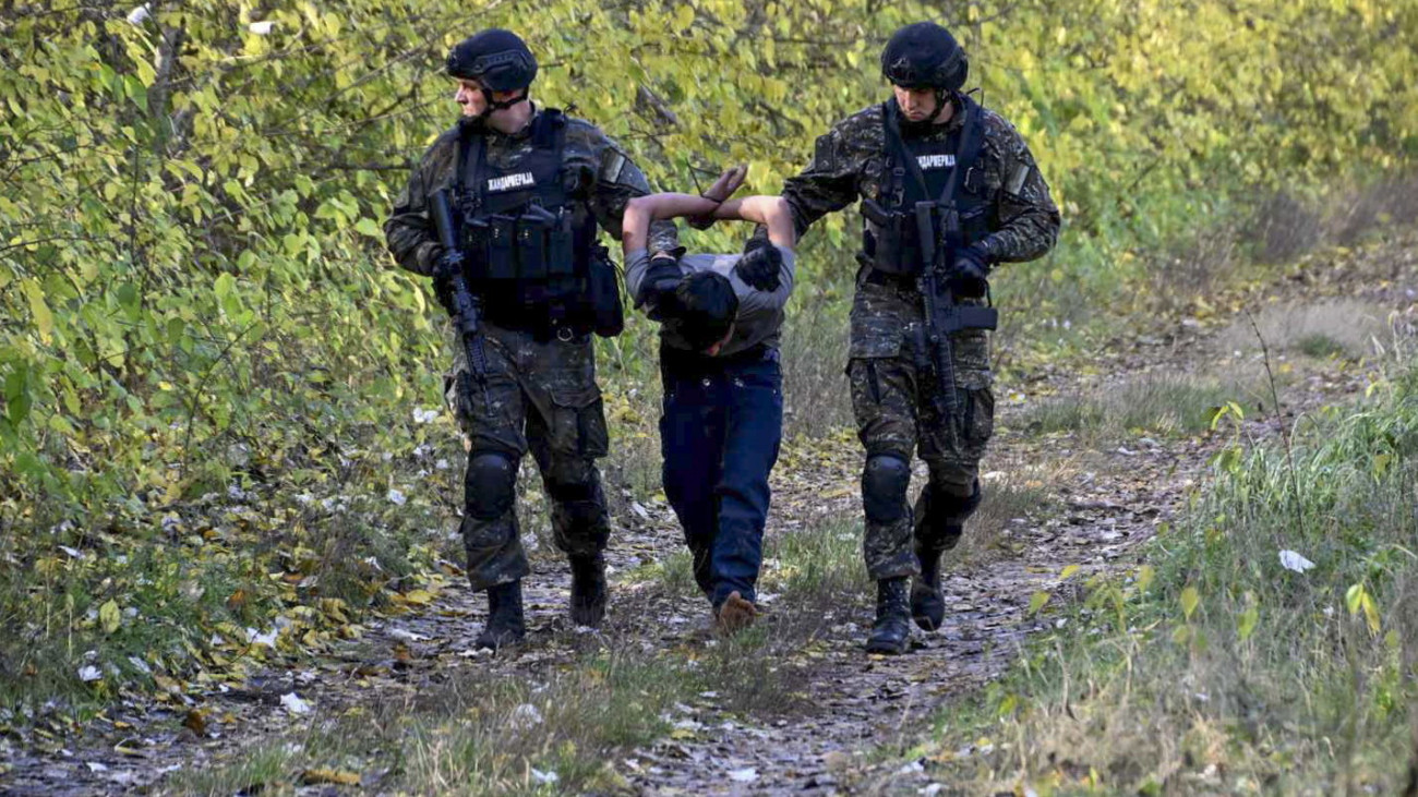 Horgos, 2023. október 30.A szerb belügyminisztérium által közreadott felvételen szerb rendőrök elvezetnek egy őrizetbe vett migráns férfit a magyar határnál levő Horgosnál 2023. október 29-én. A szerbiai hatóságok több száz rendőrt vezényeltek a Magyarországgal közös határszakaszra azt követően, hogy október 27-én hajnalban lövöldözés tört ki migránsok között Horgosnál. A három halálos áldozatot követelő incidenssel összefüggésben hat migránst állítottak elő, négyen afgán, ketten török állampolgárnak vallották magukat. A szerb-magyar határ mentén több ezer migráns vár arra, hogy átszökhessen az Európai Unióba.