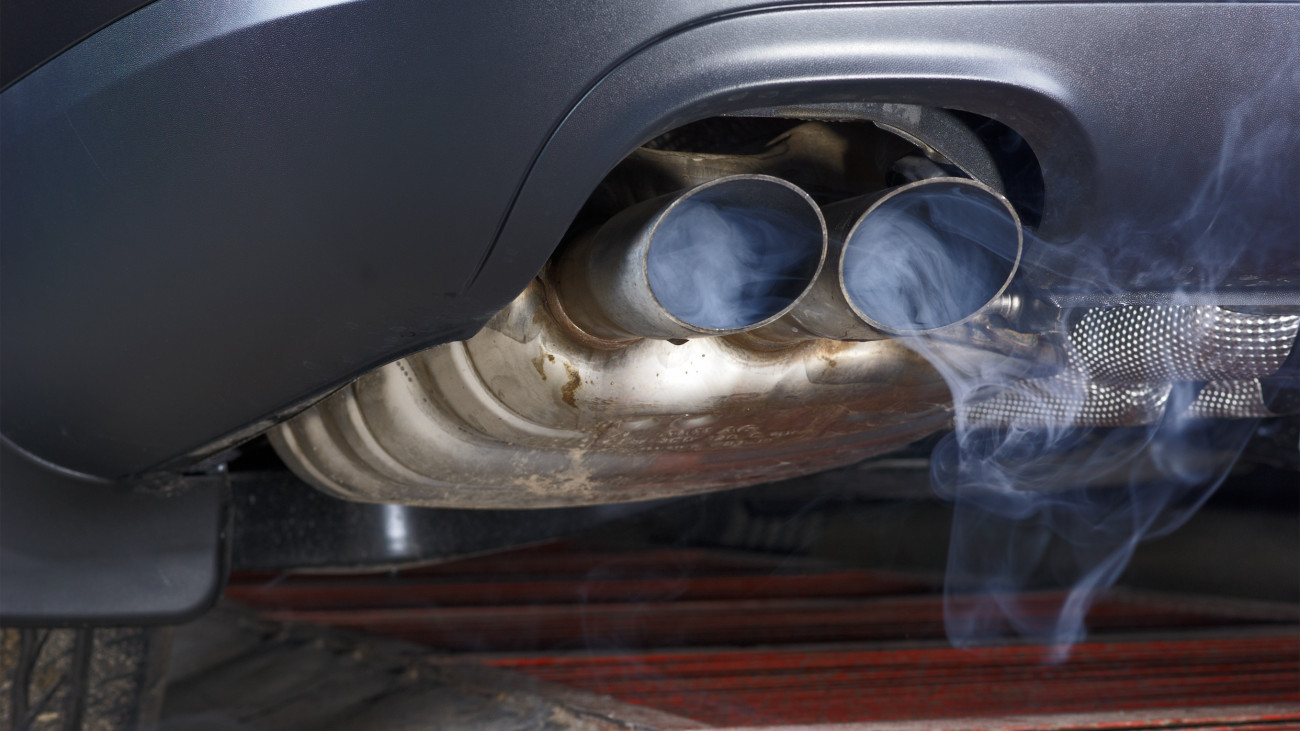 Exhaust pipe of a car - blowing out the pollution. Exhaust pipe coming out of the car with its exhaust. View from below, see the bottom of the exhaust pipe silver. Visible rear bumper eclipse of gray.