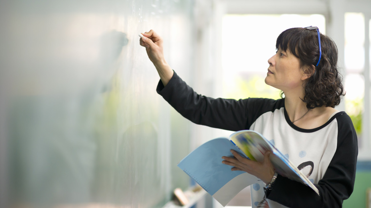 Female teacher is teaching and writing on chalkboard