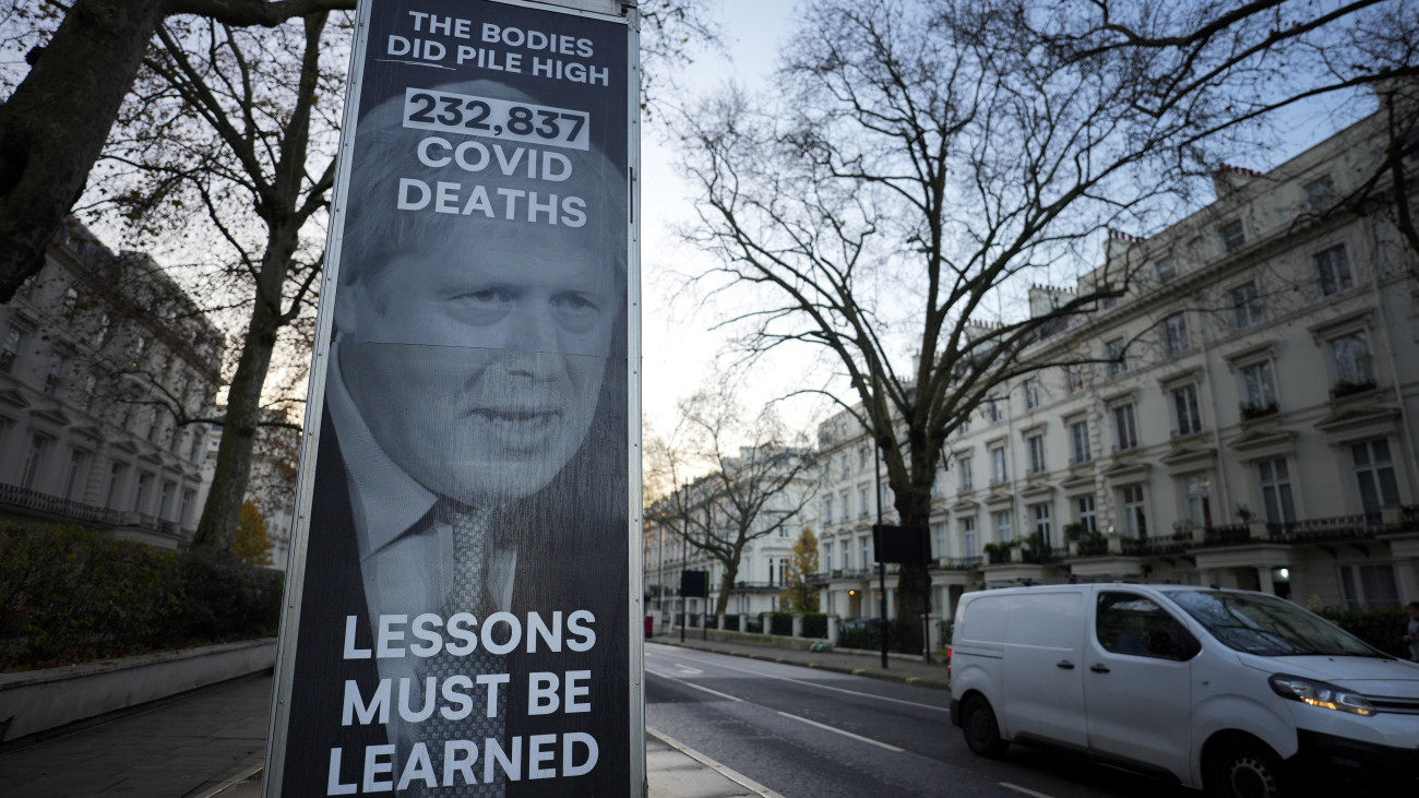 Boris Johnson volt brit miniszterelnök képe egy londoni plakáton 2023. december 6-án.  A koronavírus-járvány kezelését vizsgáló bizottság ezen a napon hallgatja meg a volt kormányfőt. A feliratok jelentése: a holttestek tényleg magasra halmozódtak - 232 837 Covid okozta halál - a leckéket meg kell tanulni. A feliratok egy Johnsonnak tulajdonított kijelentésre - hadd halmozódjanak magasra a holttestek - utalnak, amelyet állítólag a kijárási korlátozások újbóli bevezetésének felvetésére válaszul mondott.