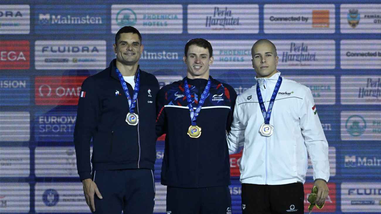 A holtversenyben második helyezett Szabó Szebasztián (j) és a francia Florent Manaudou (b), valamint a győztes brit Benjamin Proud (k) a férfi 50 méteres gyorsúszás eredményhirdetésén a rövidpályás úszó Európa-bajnokságon a romániai Otopeniben 2023. december 7-én.