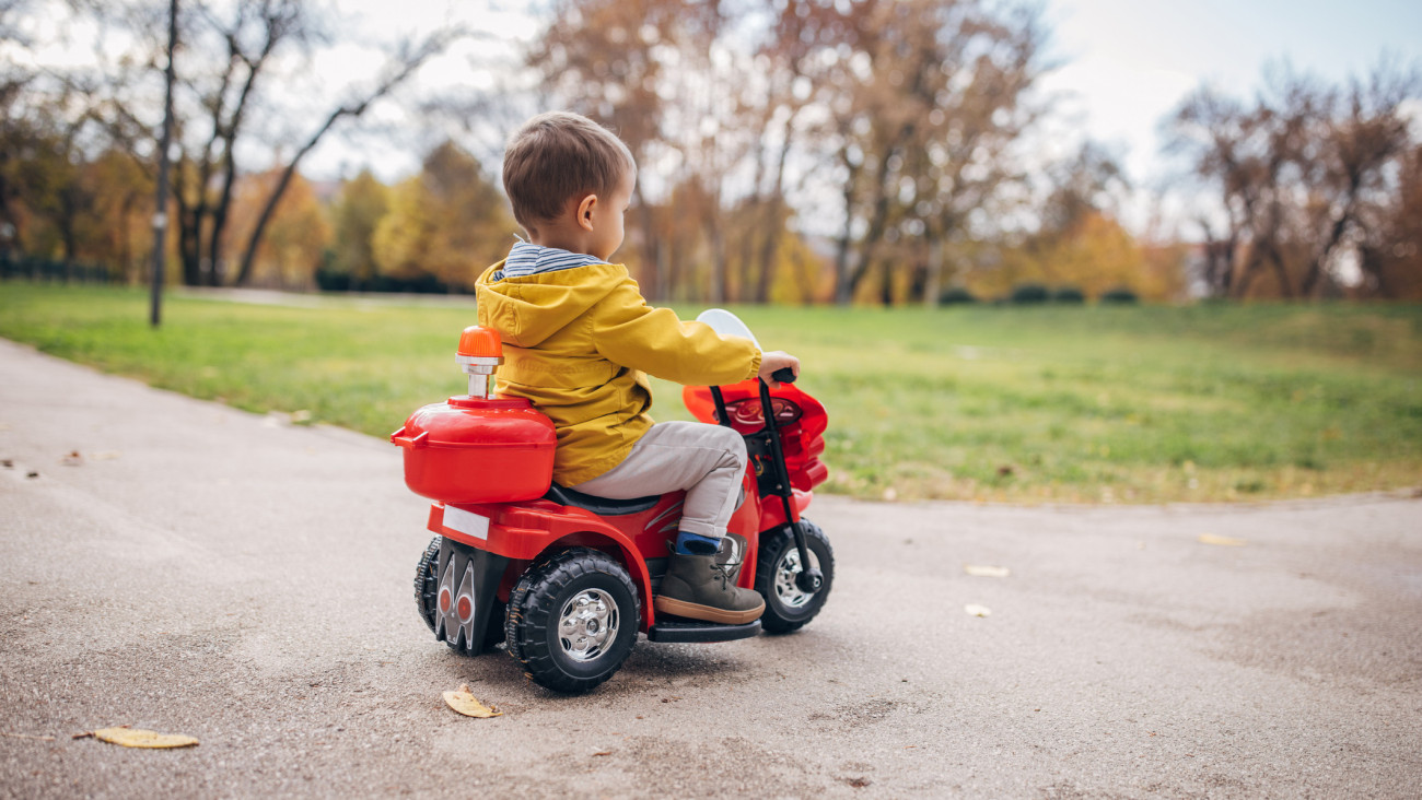 One boy, little boy ridding his toy motorcycle on autumn day in park.