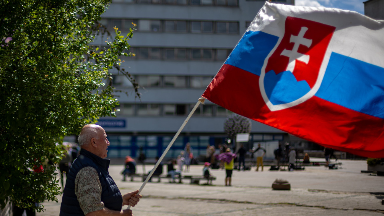 A szlovák zászlót lengeti egy férfi a Robert Fico szlovák miniszterelnököt ápoló besztercebányai F. D. Roosevelt Kóház előtt 2024. május 16-án. Fico állapota stabil, de továbbra is nagyon súlyos, miután az előző nap Nyitrabányán több lövéssel életveszélyesen megsebesítette egy 71 éves lévai férfi.