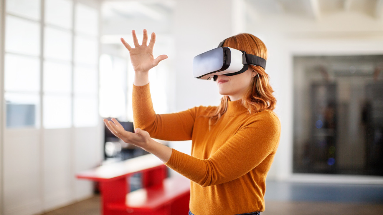 Young businesswoman using VR goggles and gesturing in office. Woman in casuals using virtual reality glasses in office.