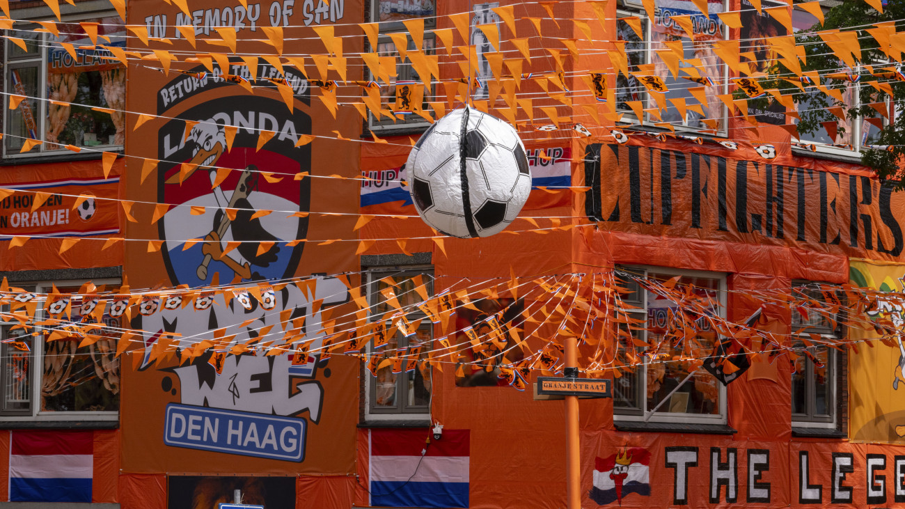 Narancssárga anyaggal bevont házak előtt egy nagy futball-labda és narancssárga zászlócskák a hágai Marktwegen 2024. június 13-án, a németországi labdarúgó Európa-bajnokság kezdete előtti napon. A Marktweg egyike azoknak a hollandiai utcáknak, amelyek hagyományosan az uralkodócsalád színeibe öltöznek, amikor a Holland labdarúgó-válogatott világ- vagy Európa-bajnokságon játszik.