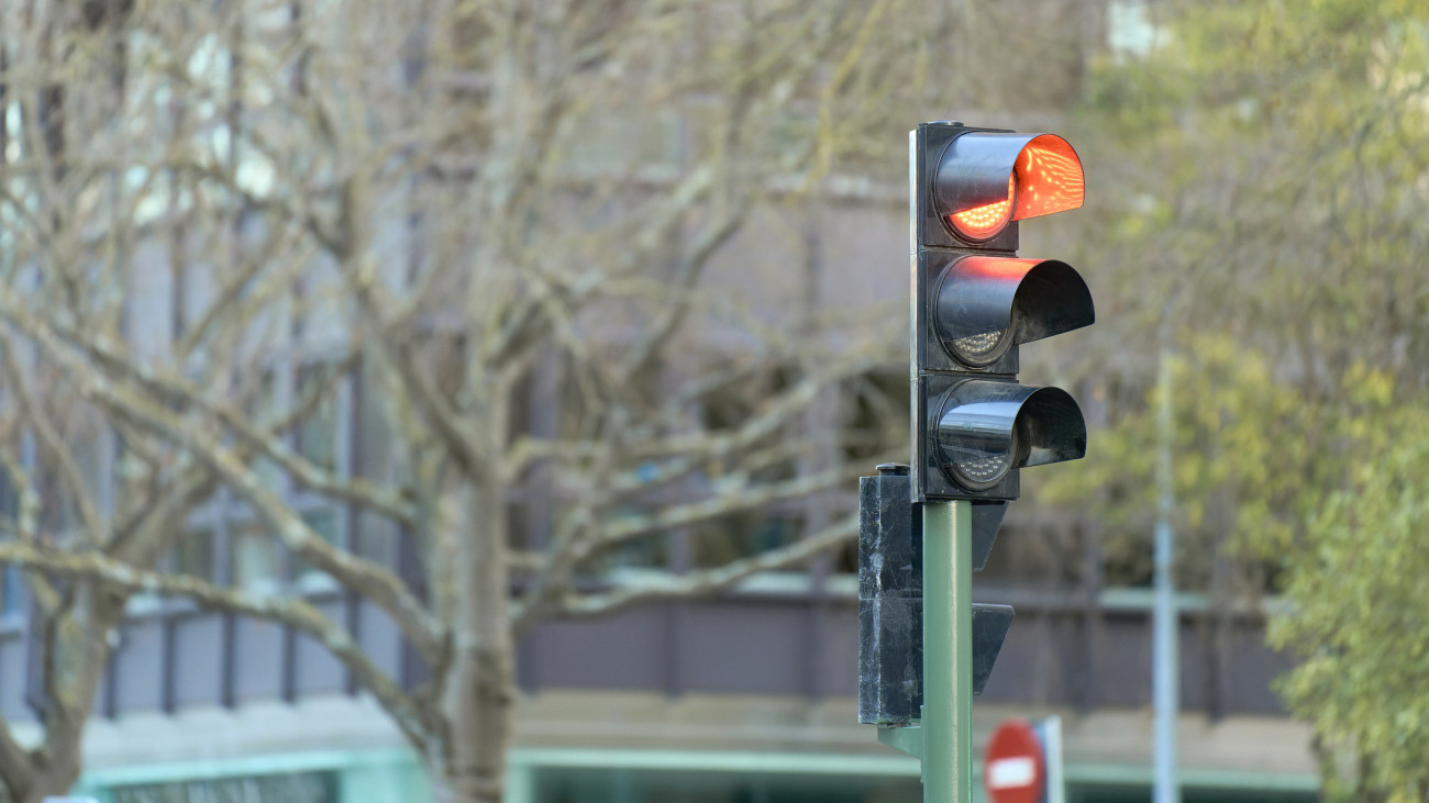 közlekedési lámpa jelzőlámpa  // Red traffic light on at street intersection, leafless trees and buildings in the background.