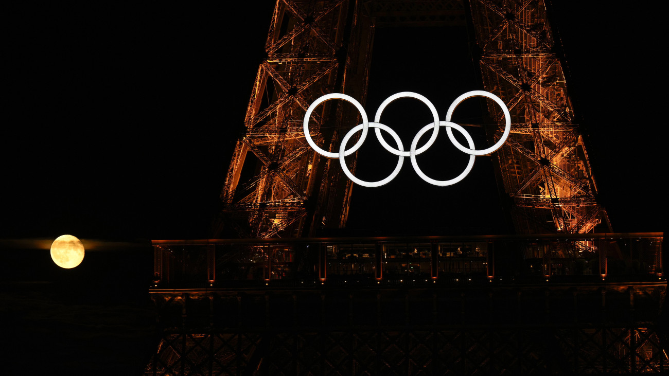 A Hold világít az olimpiai jelképpel díszített párizsi Eiffel-torony mögött 2024. július 22-én, négy nappal a párizsi nyári olimpia kezdete előtt.