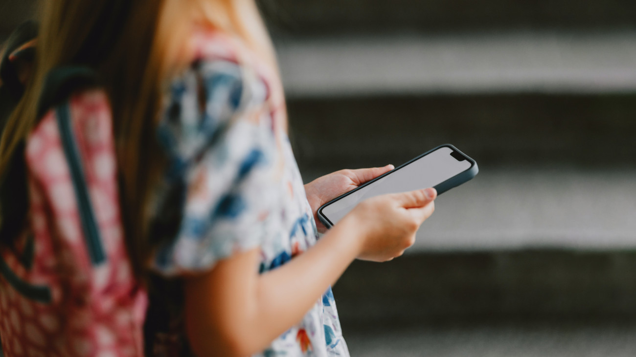 Young girl with a backpack holding a smartphone. Back to school concept showcasing technology and education.