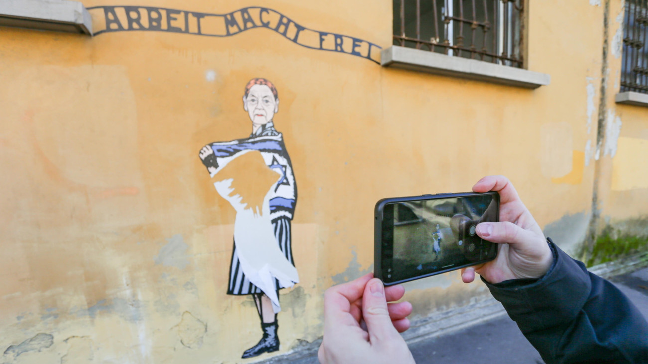 Fotót készít mobiltelefonjával egy férfi AleXsandro Palombo olasz művész Bruck Edith magyar származású olasz írót, holokauszttúlélőt ábrázoló falfestményéről, amelyet antiszemita támadás ért Milánóban 2025. február 3-án.