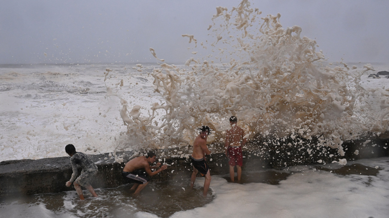 A Korall-tenger magasra csapó hullámainak habjában mártóznak meg emberek az ausztráliai Gold Coastban 2025. március 7-én. A térséghez nagy széllökésekkel, esővel és óriási hullámokkal közelítő Alfred trópusi ciklon érkezése miatt Queensland és Új-Dél-Wales államban már több ezer embert evakuáltak otthonaikból.