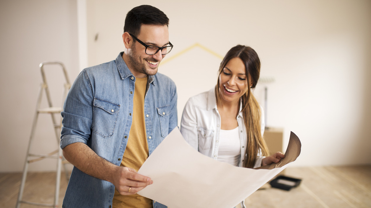 Young smiling couple in their new apartment holding and looking at blueprint.