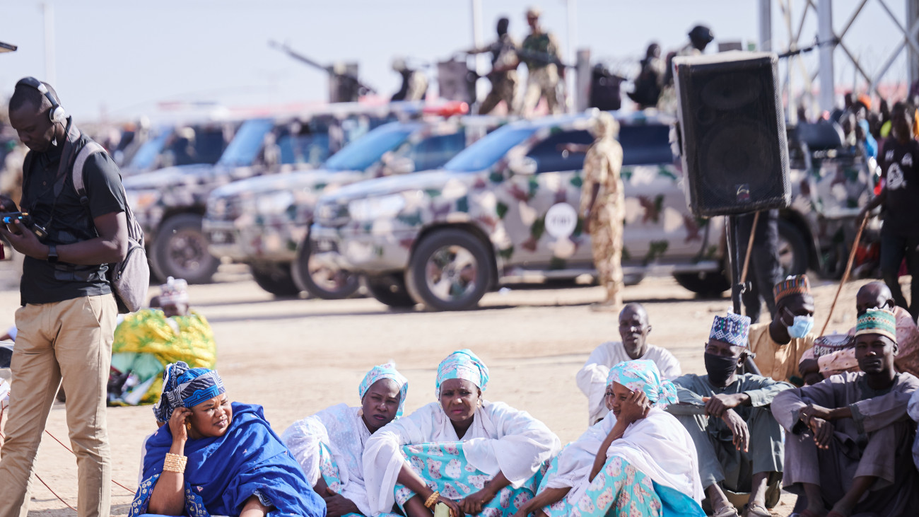 19 December 2022, Nigeria, Ngarannam: Women from Ngarannam sit on the ground while security forces stand on their cars as Foreign Minister Baerbock visits the village of Ngarannam. Ngarannam was rebuilt after being almost completely destroyed by Boko Haram, partly with German funds. Photo: Annette Riedl/dpa (Photo by Annette Riedl/picture alliance via Getty Images)