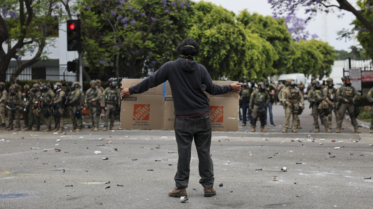 Feliratot mutat rendfenntartóknak egy tiltakozó az amerikai Bevándorlás- és Vámvégrehajtás (ICE) (ICE) elleni, erőszakossá fajult tüntetésen a kaliforniai Paramountban 2025. július 7-én, egy Los Angelesben illegális bevándorlók ellen végzett hatósági kitoloncolási művelet másnapján. Donald Trump amerikai elnök a Nemzeti Gárda egységeit küldte Los Angeles körzetébe az erőszak megfékezésére.