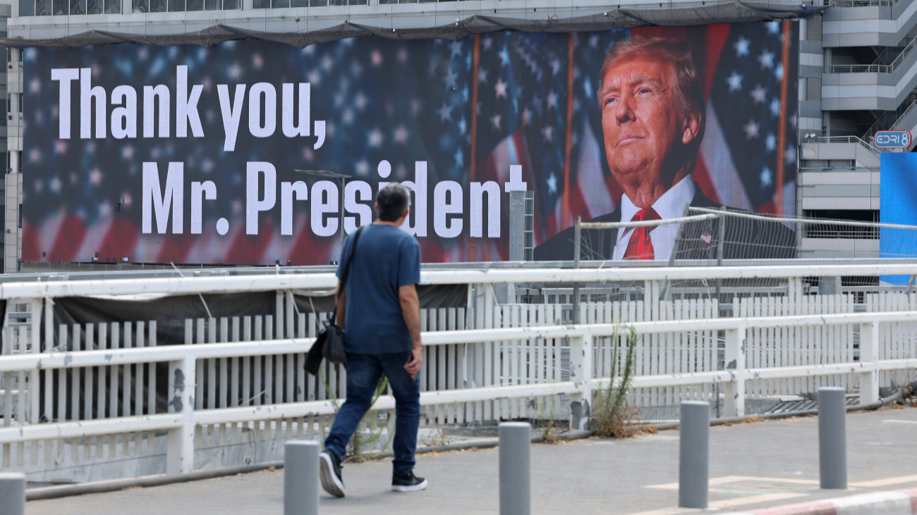 Férfi halad el Donald Trump amerikai elnököt ábrázoló óriásplakát előtt Tel-Avivban 2025 június 22-én. A felirat jelentése: Köszönjük, Elnök úr! Előző este az Egyesült Államok légitámadást indított iráni atomlétesítmények ellen. 