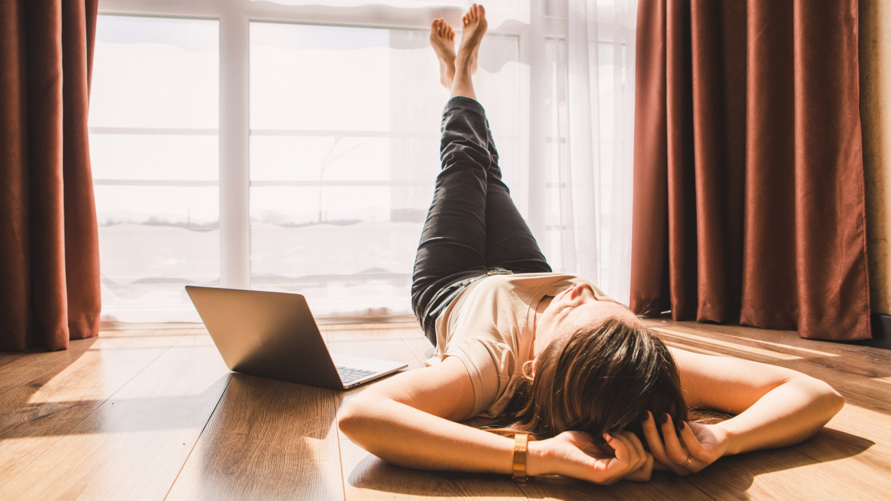 woman laying on floor of the room near big window. resting after hard work. laptop. telework
