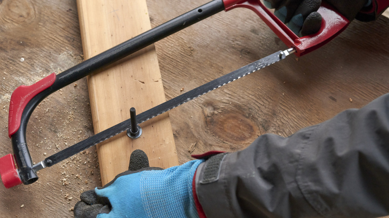 A middle-aged man cuts a bolt with a hand saw