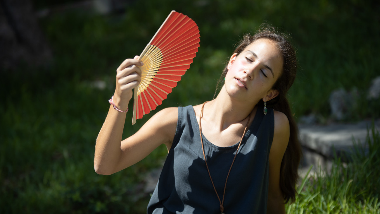 hőség kánikula nyár időjárás utazás legyező // Teenage girl sitting in the garden overwhelmed by the sun with a fan