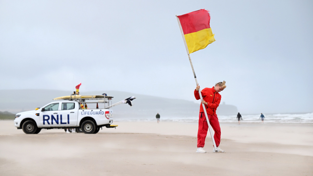 PORTSTEWART, NORTHERN IRELAND - AUGUST 4: An RNLI lifeguard battles against the strong winds on Portsteward Strand as she plants a warning flag advising swimmers against entering the water on August 4, 2025 in Portstewart, United Kingdom. The Met Office has issued an amber warning for much of Scotland and a yellow warning for northern England, north Wales and Northern Ireland, as Storm Floris threatens the northern half of the UK with strong winds and heavy rains on Monday and into Tuesday. Storm Floris is the sixth named storm of the 2024-25 season, following Storm Eowyn in January.  (Photo by Charles McQuillan/Getty Images)