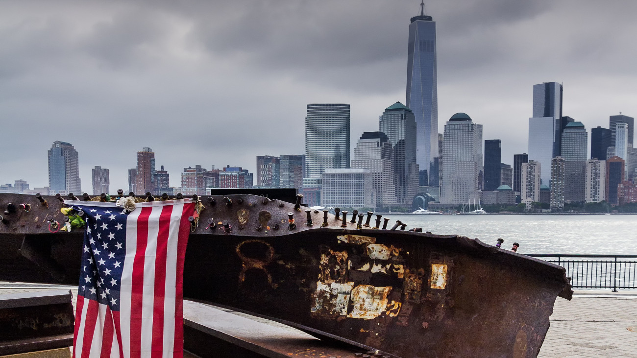 A steel girder from one of the fallen World Trade Center Towers, across the Hudson river from Manhattan. An American Flag is draped over the girder with the Freedom Tower in the background.
