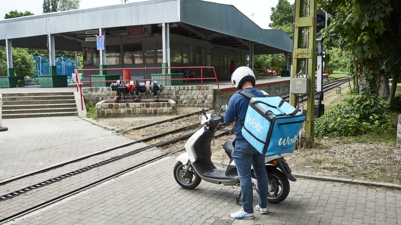 Budapest, 2023. május 29. A Wolt elnevezésű, éttermekkel szerződött kerékpáros ételfutár a megrendelt ételt melegentartó táskával várakozik a fogaskerekű vasút, a Budapesti Közlekedési Központ (BKK) 60-as számú járatának városmajori végállomásánál. MTVA/Bizományosi: Róka László
