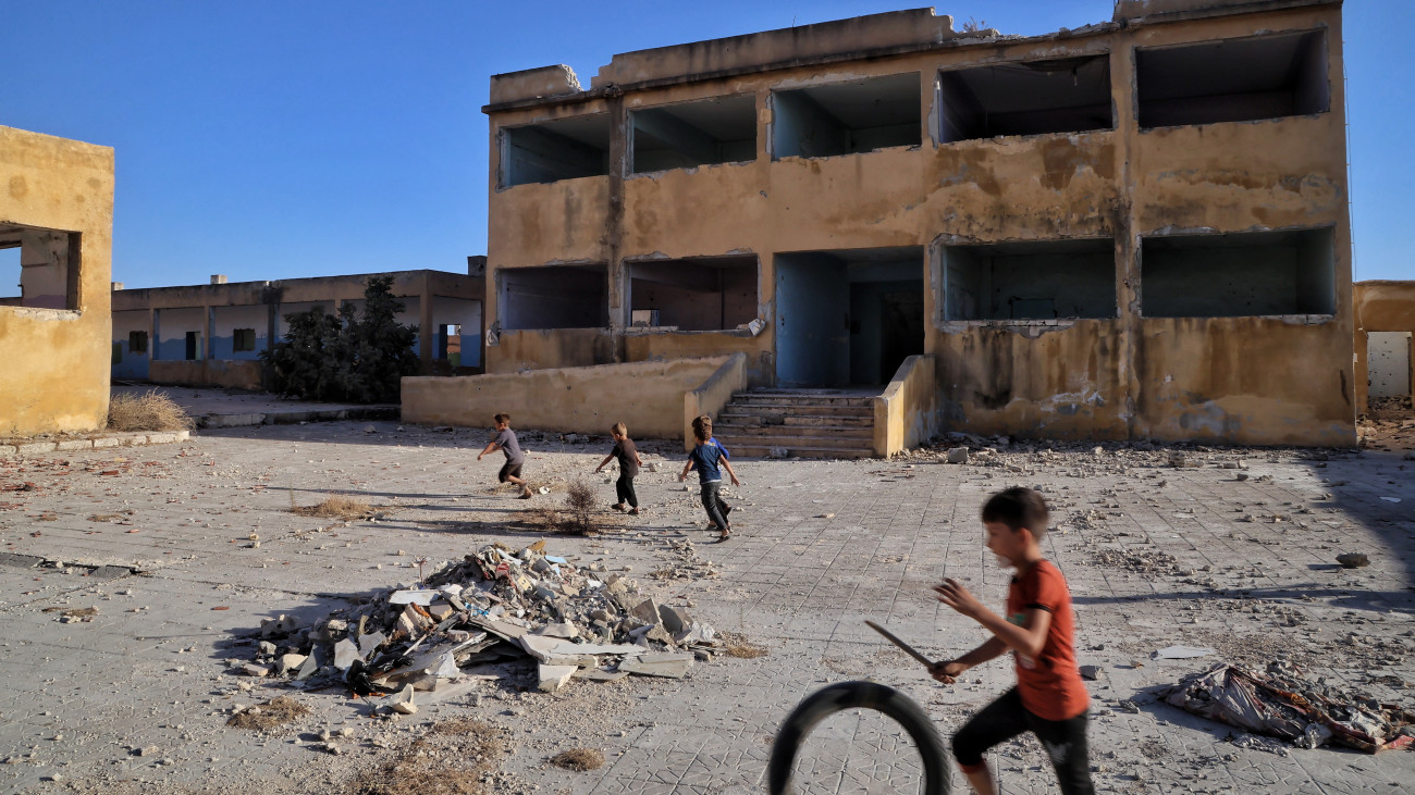 Fiúk játszanak egy megrongálódott iskolaépület udvarán az Idlíb szíriai tartomány déli részén levő Hasszban 2025. szeptember 21-én, az új szíriai tanév kezdőnapján. Az ország oktatási minisztériuma szerint négymilliónál több diák kezdte meg a 2025-26-os tanévet, az iskolaépületek közel felét azonban újra kell építeni az Aszad-rezsim 2024. decemberi bukását eredményező, tizenhárom évnyi polgárháború után.