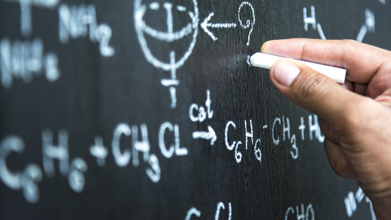 Teacher writing the physics formula on black board in school classroom, School education concept