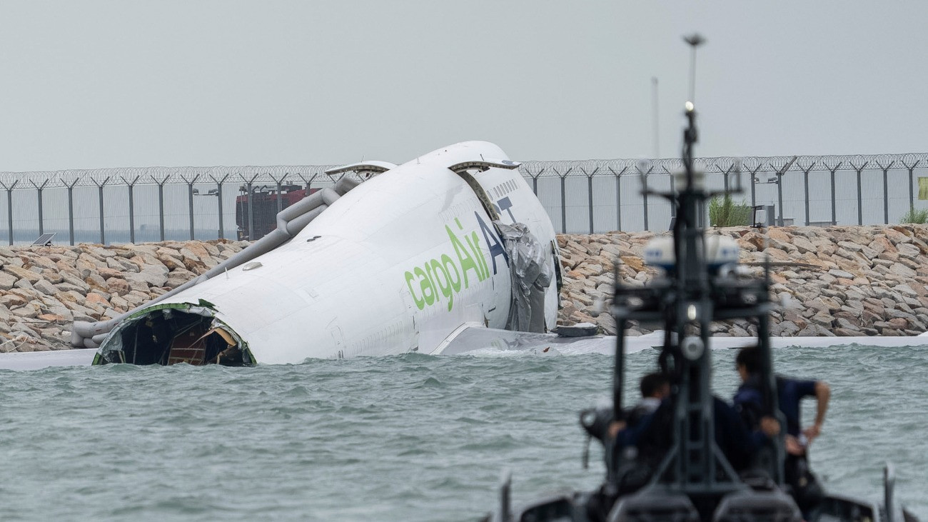 Mentõalakulatok tagjai egy megrongálódott teherszállító repülõgépnél a hongkongi repülõtéren 2025. október 20-án. A Boeing 747-es típusú gép landoláskor kicsúszott a leszállópályáról, ütközött egy biztonsági járõrkocsival, a tengerbe lökte a jármûvet, majd a vízbe zuhant és részben elmerült. A balesetben két hongkongi repülõtéri biztonsági alkalmazott életét vesztette, a fedélzeten tartózkodó négyfõs legénység mindegyik tagja megmenekült.