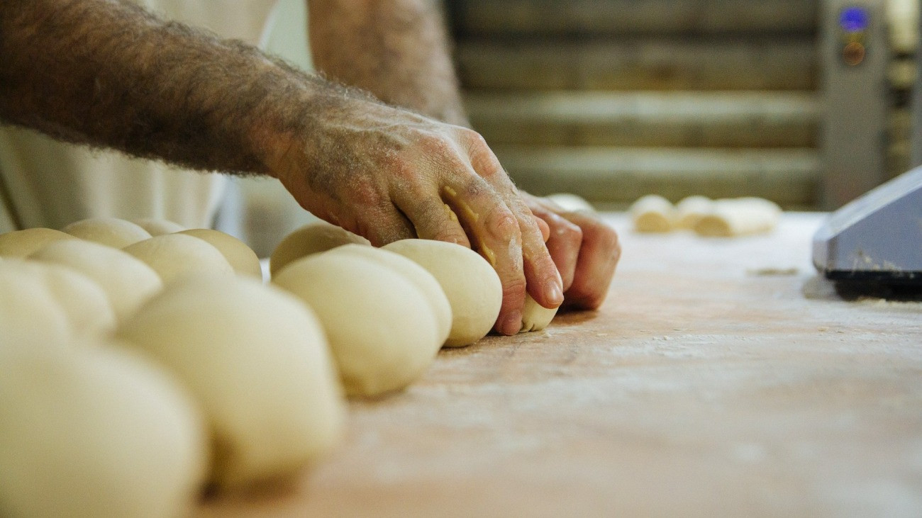 Egy pék tésztát gyúr egy sütödében.