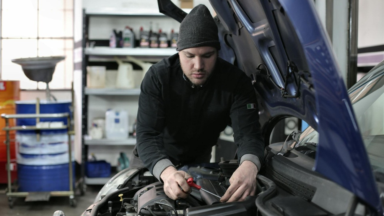 Egy autószerelő egy autó motorján dolgozik.