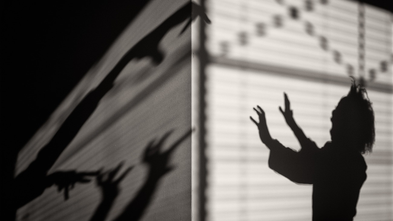 Rémisztő kezek árnyéka ijeszt egy leányt, akiből szintén az árnyképe látszik, miközben a kezeit védekezőn maga elé emeli.