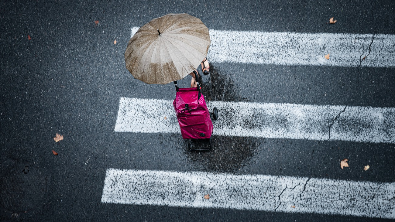 Gyalogos kel át egy zebrán szakadó esőben, kezében egy esernyővel.Forrás: Getty Images/fcafotodigital