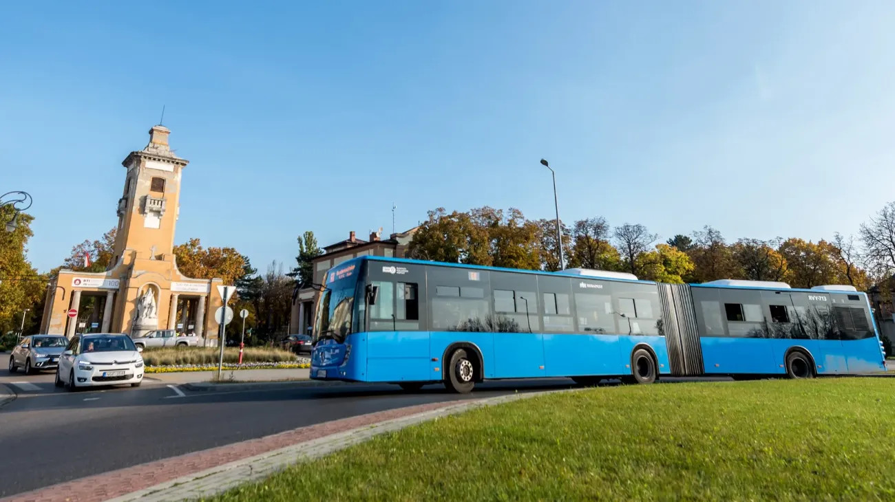 A budapesti közösségi közlekedés ikonikus járműve, egy kék színű csuklós autóbusz fordul a fővárosi Új köztemető előtt. A temető bejáratának impozáns épületét Hegedűs Ármin tervezte 1903-ban.