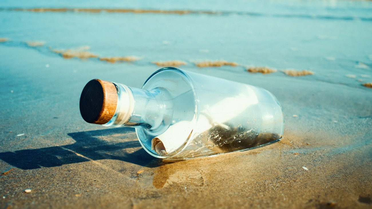 Üvegpalackba zárt, papírra vetett üzenet hever egy napsütötte tengerpartonGetty Images/SEAN GLADWELL