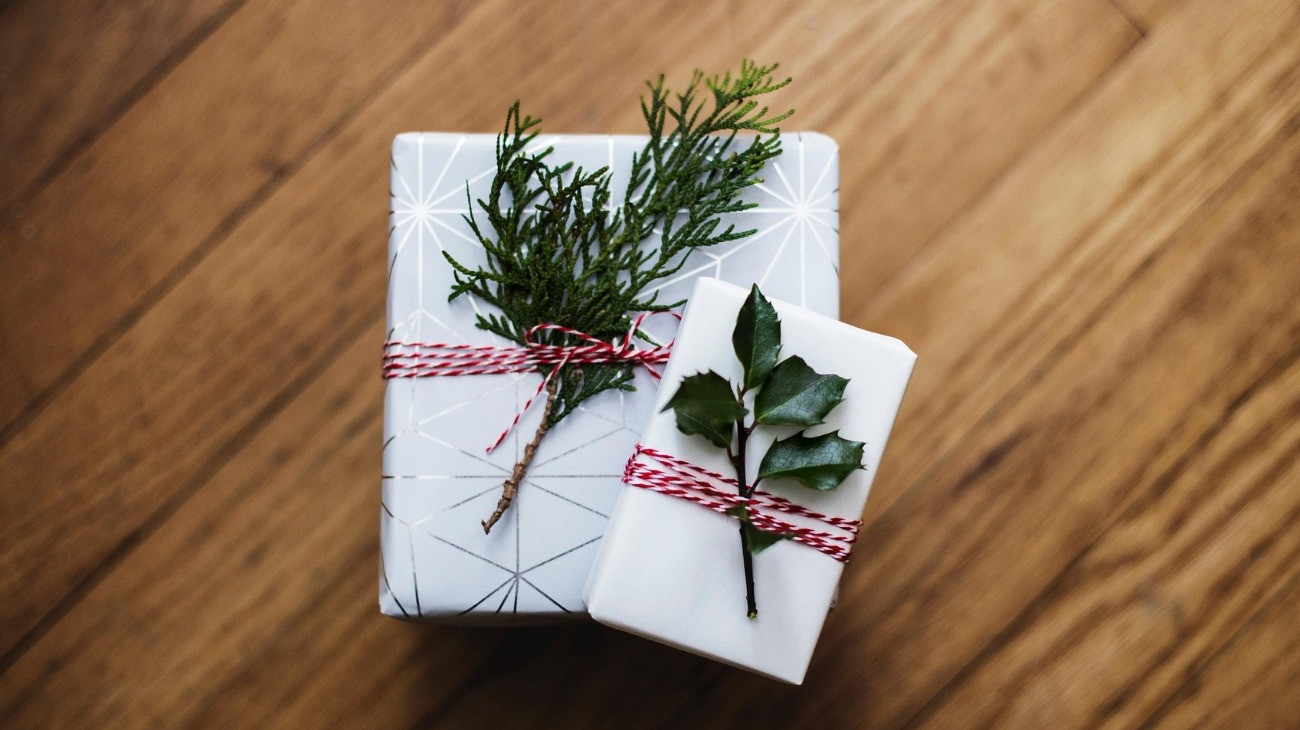 Kisebb dobozokba csomagolt karácsonyi ajándékok növényi díszítéssel, parkettán elhelyezve.