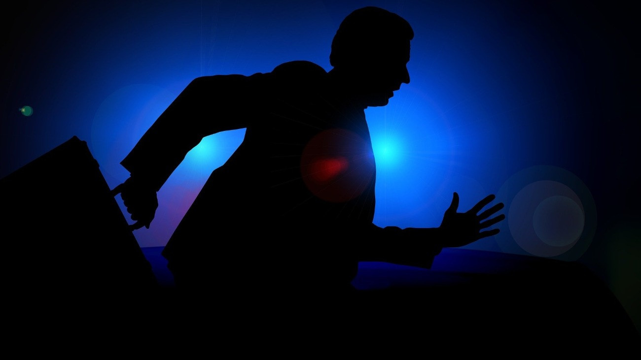 Öltönyös férfi futva erőlködik, aktatáskával, a háttérben sejtelmes kék fény.