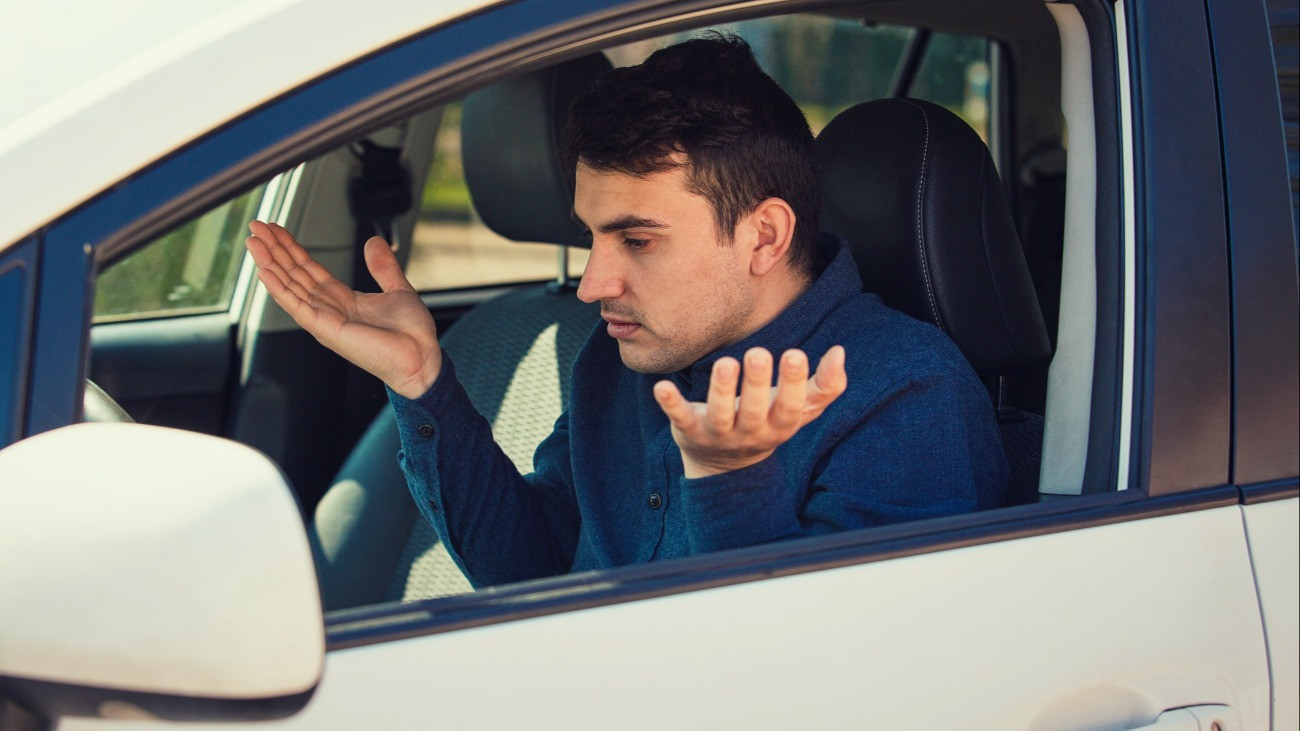 Angry young man driver, pissed off shaking hands and shrugging shoulders, has problems with the car. Displeased perplexed guy has a road accident. Traffic jam rush hour.