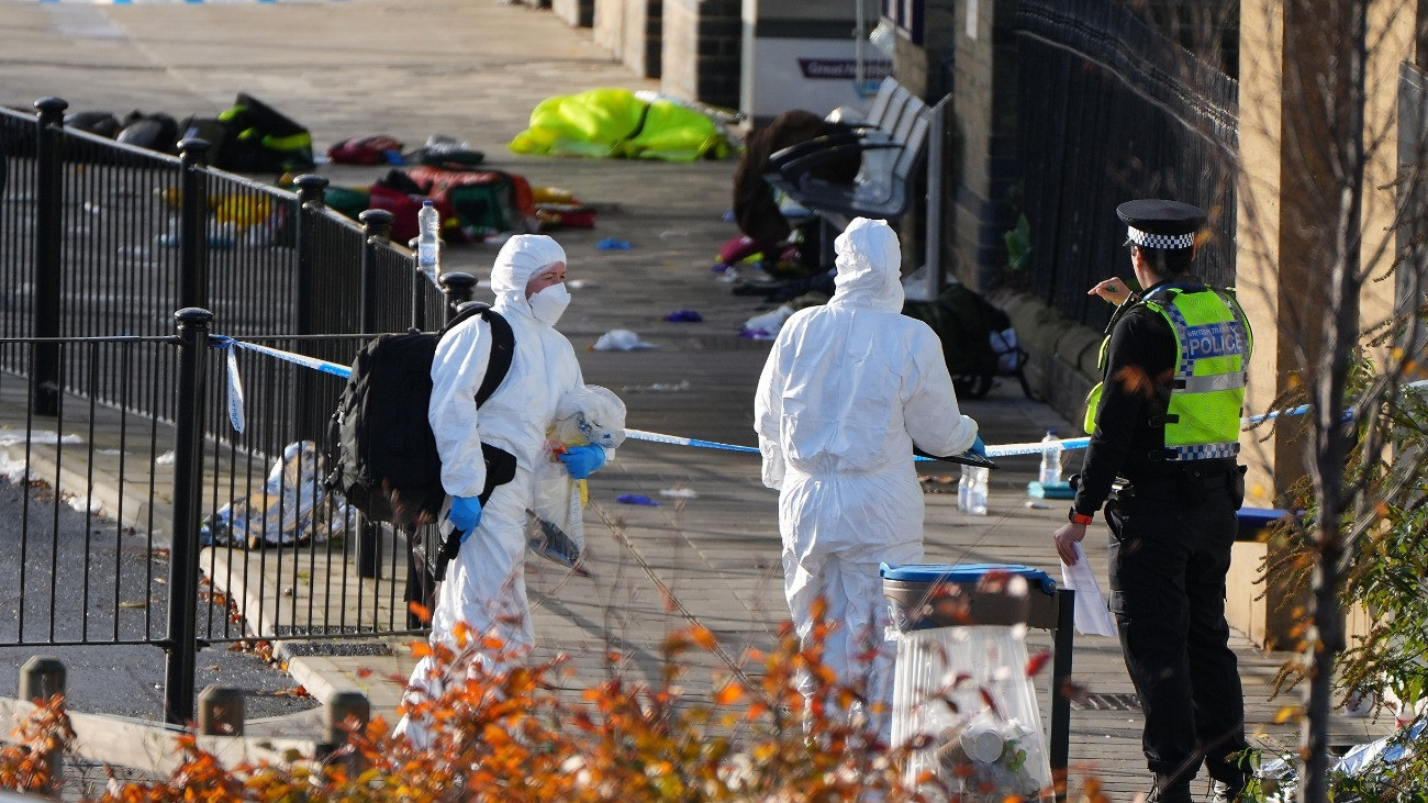 Helyszínelõ rendõrök a menekülõ utasok által hátrahagyott holmik elõtt, a Cambridgeshire megyében fekvõ Huntingdon vasútállomásán 2025. november 2-án, miután a közelben késes támadás történt egy Londonba tartó vonaton. Tízen megsérültek, közülük kilencen életveszélyesen. A két brit állampolgár támadót õrizetbe vették. A rendõrség nem terrorcselekménynek tekinti a támadást.