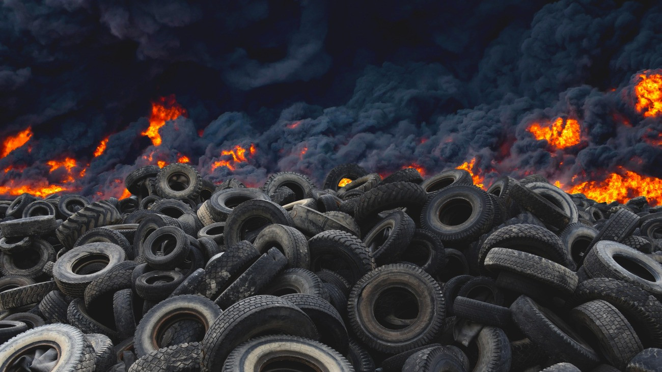 Tyres are on fire. Burning old tyres on recycling landfill. Black smoke from tires fire. Tyre graveyard at rubber burning plant. Wheel tire recyclers, tyre for reuse. Pile of old wheels in blaze.