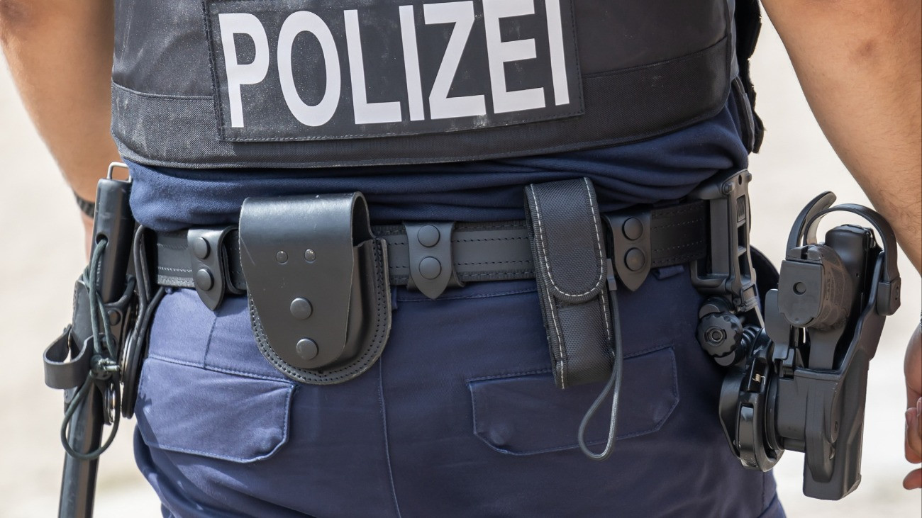 Német rendőr hátulról, a derékszíján különböző rendfenntartó eszközök lógnak, jobb oldalán a kézifegyvere látható.