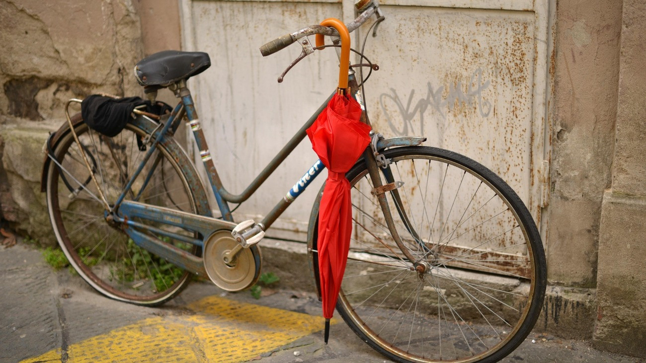 Piros esernyő lóg egy rossz állapotban lévő kerékpár kormányán.