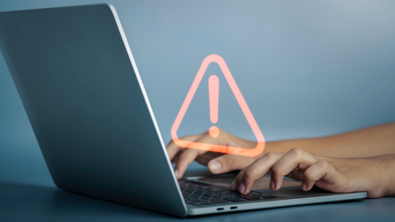 Háromszög alakú figyelmeztető tábla egy laptop képernyője előtt.