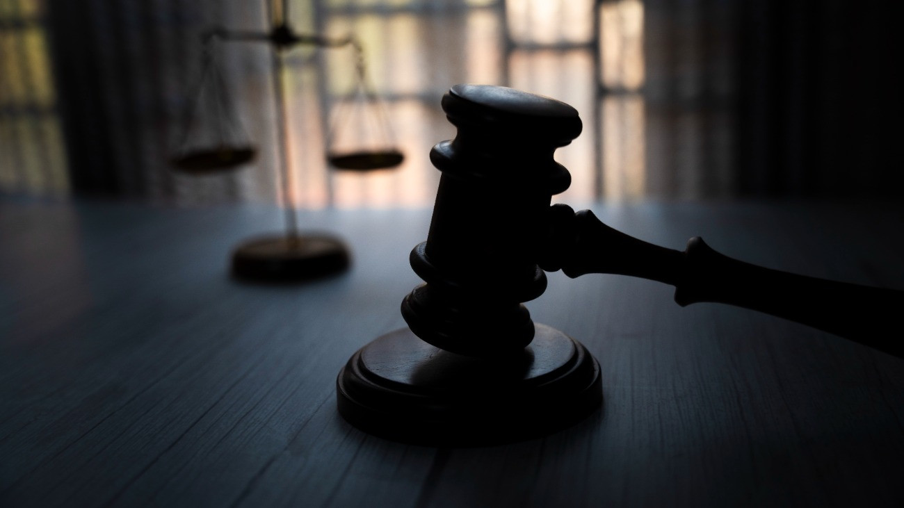 Fából készült bírói kalapács egy asztalon, háttérben egy mérleggel, ami a mérlegelés, bíráskodás, megítélés, kiegyensúlyozás, a kiegyensúlyozottság, az igazságosság és az okos belátás jelképe